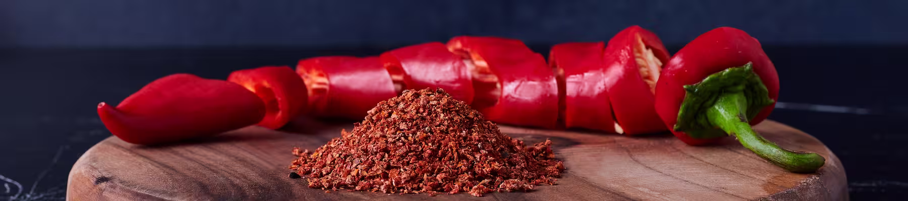 Chopped red chili pepper and smoked paprika powder on a wooden plate on a black table