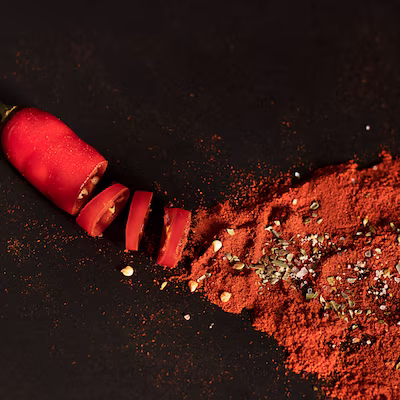 Smoked paprika powder with pepper seeds beside a chopped pepper on a dark surface