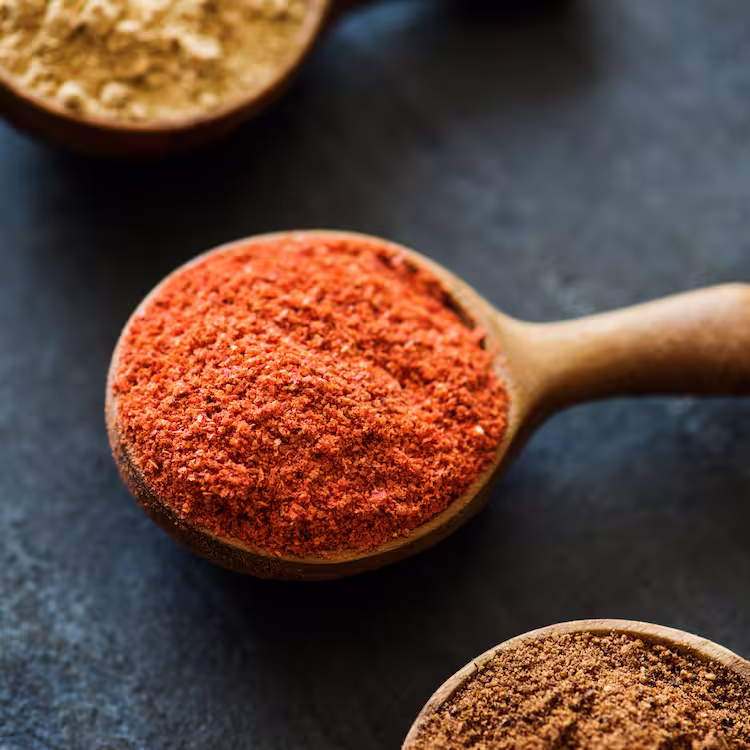 Flavourful smoked paprika powder in the midst of two other spices on a black table